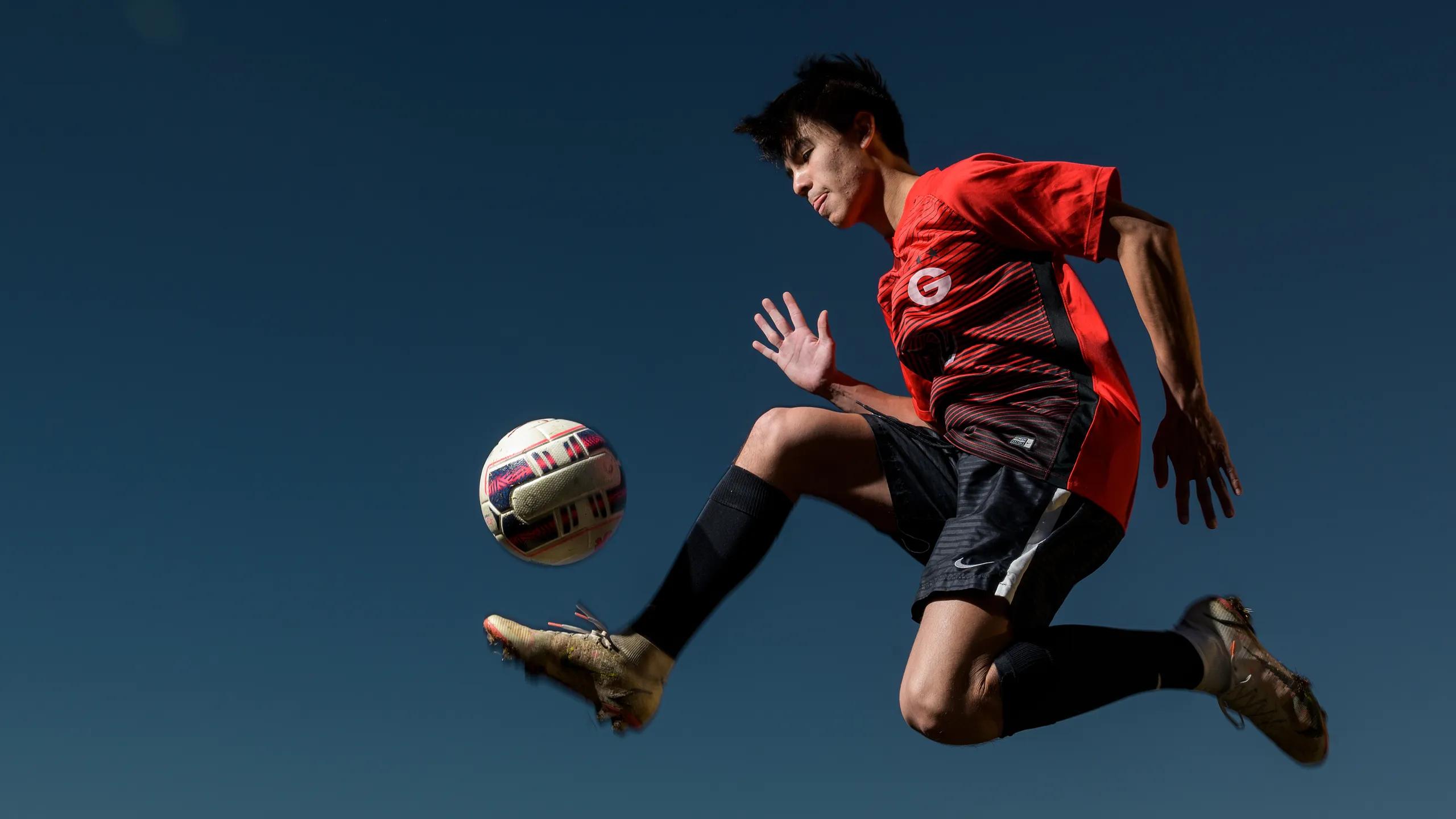 A player in a red kit volleys a ball in mid-air