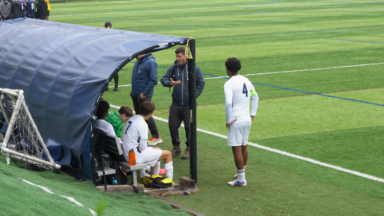 A coach talking with a player beside the team bench during a match